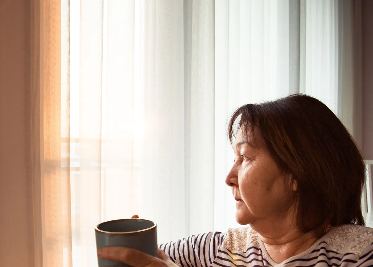 Vrouw zit met een mok thee bij het raam en kijkt rustig naar buiten